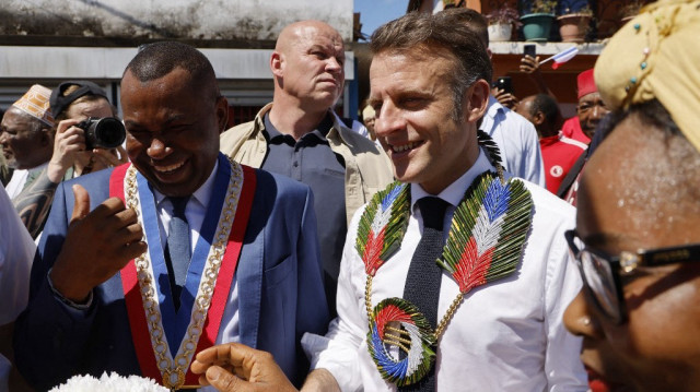 Le président français Emmanuel Macron (à droite), entouré du maire de la ville Issilamou Hamada, est accueilli avec des fleurs à son arrivée à l'hôtel de ville lors d'une visite dans le territoire français d'outre-mer de Mayotte touché par le cyclone, à Tsingoni, le 21 avril 2025.