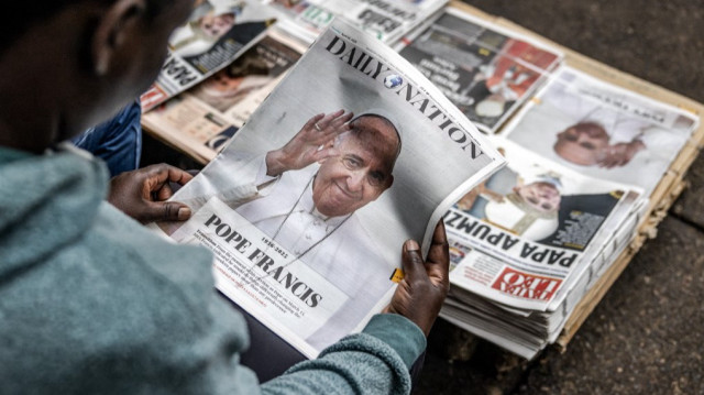 Une femme est assise à un kiosque à journaux dans la rue pour lire les premières pages portant des titres et des images annonçant la mort du pape François, dans le centre de Nairobi, le 22 avril 2025, un jour après son décès.
