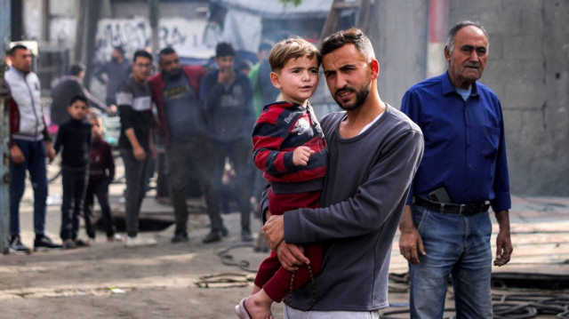 Un homme porte un enfant avec d'autres personnes alors qu'ils inspectent les dégâts au garage de la municipalité de Jabalia, qui a été touché par un bombardement israélien, à Jabalia dans le nord de la bande de Gaza, le 22 avril 2025.