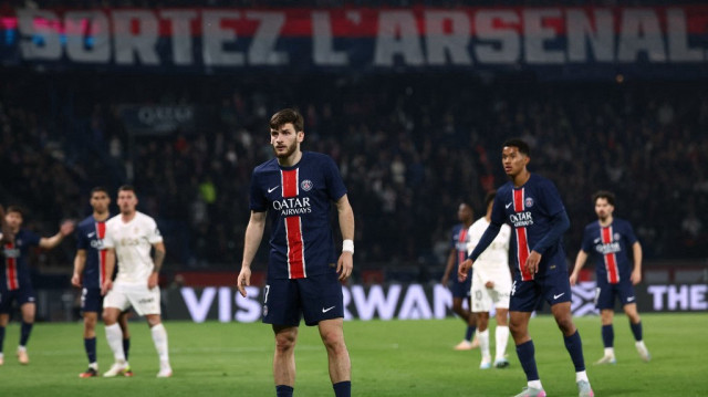 L'attaquant géorgien du Paris Saint-Germain Khvicha Kvaratskhelia se tient sur le terrain tandis que les supporters du Paris Saint-Germain brandissent une bannière sur laquelle il est écrit "Sortez l'Arsenal" lors du match de football de Ligue 1 entre le Paris Saint-Germain (PSG) et l'OGC Nice au stade du Parc des Princes à Paris, le 25 avril 2025.