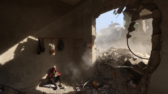 Un garçon palestinien tient un livre alors qu'il est assis dans les décombres d'une maison, suite aux frappes israéliennes de la nuit, dans le camp de réfugiés de Nuseirat, dans le centre de la bande de Gaza, le 29 avril 2025. 