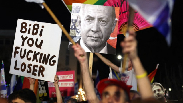 Un manifestant tient une pancarte avec les portraits du Premier ministre israélien Benjamin Netanyahu lors d’un rassemblement contre les tentatives du gouvernement israélien de limoger la procureure générale Gali Baharav-Miara et le chef de l’agence de sécurité intérieure, Ronen Bar, sur la place Habima à Tel Aviv, le 27 mars 2025.
