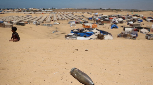 Un obus non explosé repose sur une dune de sable alors qu'un jeune garçon est assis près d'un camp de fortune pour les Palestiniens déplacés dans la zone de Tel al-Sultan à Rafah dans le sud de la bande de Gaza le 30 mai 2024,