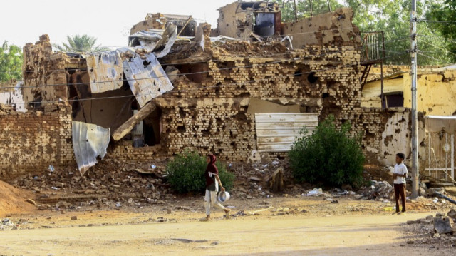 Un garçon soudanais regarde une femme passer devant un bâtiment endommagé à Omdurman, ville jumelle de Khartoum, le 20 mars 2025.