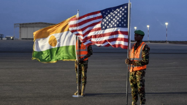Deux soldats nigériens tiennent les drapeaux américain et nigérien sur la base aérienne 101 à Niamey, le 7 juin 2024, lors de la cérémonie du premier départ des troupes américaines du Niger.
