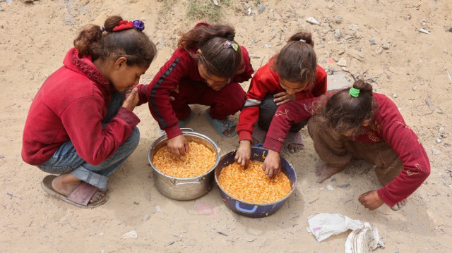 Des jeunes filles palestiniennes mangent des aliments chauds provenant de rations fournies par une cuisine de charité installée sur le campus de l'université islamique dans la ville de Gaza, le 12 mai 2025.