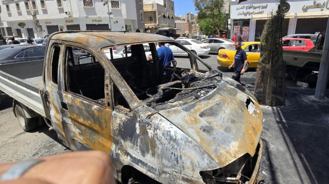 Des personnes passent devant des voitures détruites lors des affrontements de la nuit dans le quartier sud d'Abu Salim à Tripoli, capitale de la Libye, le 13 mai 2025.