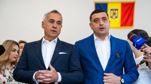 Le leader du parti nationaliste souverain Alliance pour l'Union des Roumains (AUR) et candidat à la présidence George Simion (à droite) parle à côté de l'ancien candidat à la présidence Calin Georgescu dans un bureau de vote, lors du second tour des élections présidentielles, à Mogosoaia, près de Bucarest, le 18 mai 2025. Les Roumains ont commencé à voter le 18 mai dans le cadre d'une nouvelle élection présidentielle tendue, une course serrée entre un nationaliste et un centriste qui pourrait remodeler la direction de ce pays pro-Bruxelles qui borde l'Ukraine déchirée par la guerre.