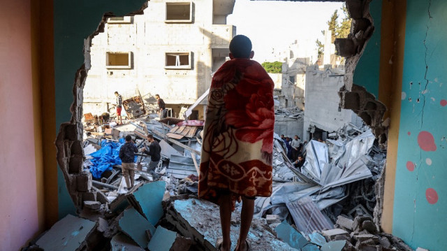 Un jeune drapé dans une couverture regarde les gens chercher des survivants dans les décombres d'un bâtiment touché par une frappe israélienne dans le camp de Bureij pour les réfugiés palestiniens dans le centre de la bande de Gaza, le 2 mai 2025.