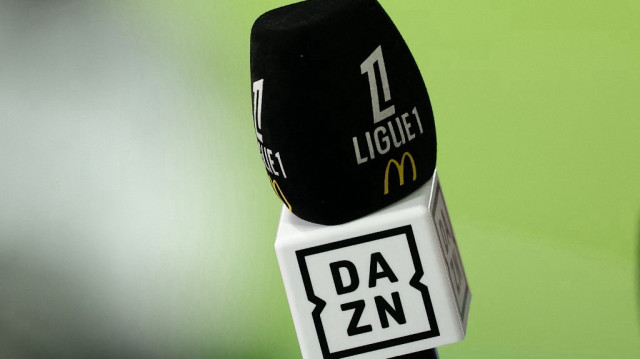 Un journaliste tient un micro arborant les logos de la Ligue 1 française et de la plateforme de streaming DAZN lors du match de Ligue 1 entre le Paris Saint-Germain (PSG) et l’OGC Nice, au Parc des Princes à Paris, le 25 avril 2025.