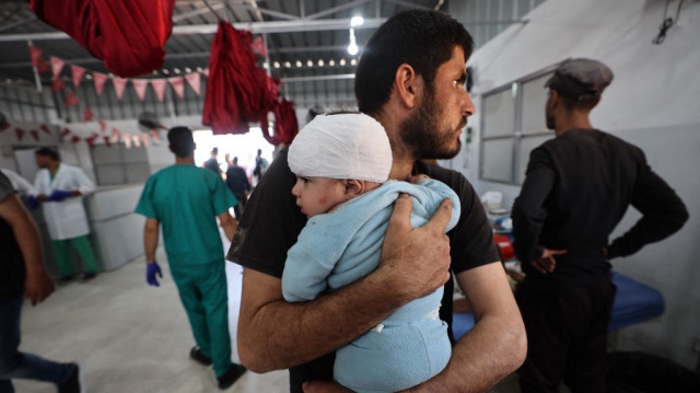 Un homme tient un enfant blessé après avoir été soigné à l'hôpital Al-Awda dans le camp de réfugiés de Nuseirat, dans le centre de la bande de Gaza, à la suite d'une frappe aérienne israélienne qui a touché une école du camp, le 19 mai 2025.