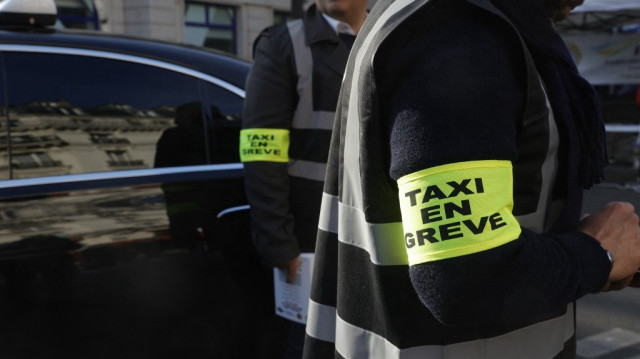 Des chauffeurs de taxi portant un brassard indiquant "Taxi en grève" à Paris le 19 mai 2025, lors d'une manifestation nationale contre les changements proposés dans la manière dont l'État finance les services de transport médical.
