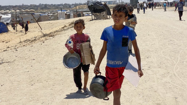 Des enfants palestiniens déplacés transportant des pots vides et des cartons reviennent d'un centre de distribution d'aide à Khan Yunis, dans le sud de la bande de Gaza, le 28 mai 2025.