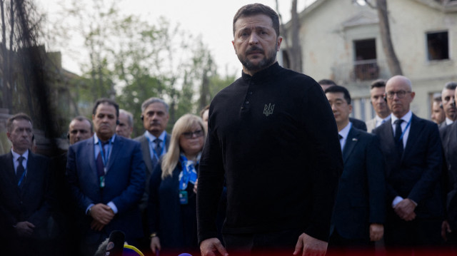 Le président ukrainien Volodymyr Zelensky s'adresse à la presse tandis que des diplomates se tiennent derrière lui près d'un immeuble résidentiel détruit à la suite d'une attaque de missiles russes à Kiev, le 25 avril 2025, dans le cadre de l'invasion russe de l'Ukraine.
