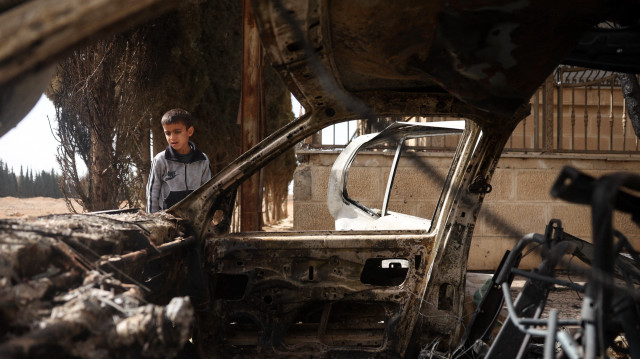 Un garçon vérifie une voiture détruite à la suite d'affrontements sectaires à Ashrafiyat Sahnaya, près de Damas, le 1er mai 2025. Le chef spirituel des Druzes syriens, le cheikh Hikmat al-Hijri, a condamné le 1er mai ce qu'il a qualifié de "campagne génocidaire" contre son peuple, après deux jours d'affrontements sectaires meurtriers.
