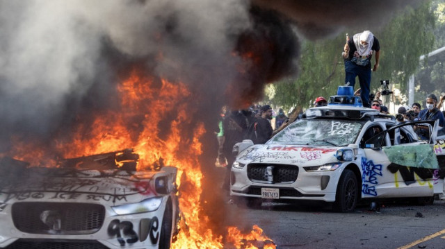 Des manifestants brisent le pare-brise d'un véhicule à côté d'un véhicule Waymo en feu alors que des manifestants affrontent les forces de l'ordre dans les rues entourant le bâtiment fédéral lors d'une manifestation à la suite des opérations fédérales en matière d'immigration à Los Angeles, en Californie, le 8 juin 2025.