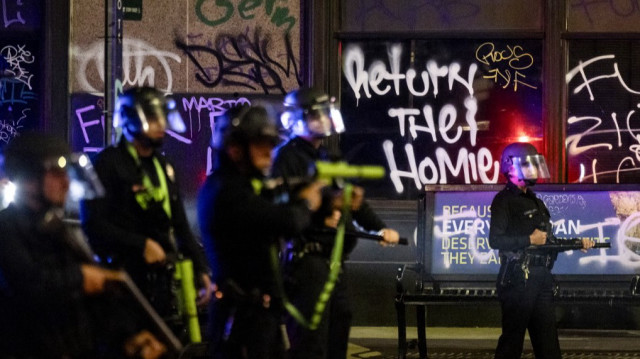 Un graffiti "Return the Homies" derrière des policiers de Los Angeles déployés à côté de l'hôtel de ville alors que les affrontements avec les manifestants se poursuivent dans la nuit lors d'une manifestation suite aux opérations fédérales d'immigration, à Los Angeles, Californie, le 8 juin 2025.