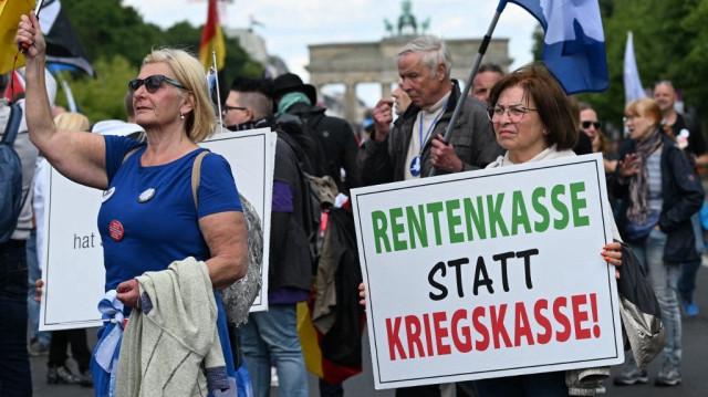 Un participant tient une pancarte sur laquelle on peut lire "Fonds de pension au lieu de trésor de guerre !" lors d'une manifestation intitulée "Frieden - Freiheit - Volksabstimmung" (Paix - Liberté - Référendum) organisée par un réseau appelé "Deutschland steht auf" (L'Allemagne se lève) comprenant des groupes d'extrême droite et des membres du mouvement dit "Querdenker" (penseurs latéraux), le 24 mai 2025 à Berlin.