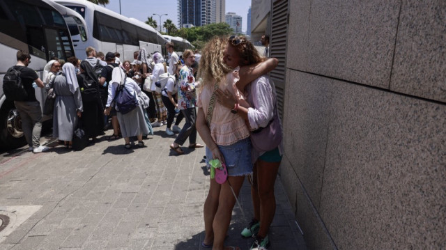 Des femmes se donnent l'accolade avant le départ d'un bus destiné à évacuer d'Israël les détenteurs de passeports étrangers, principalement européens et polonais, à un point de rencontre à Tel Aviv, le 17 juin 2025.
