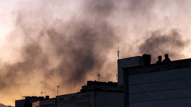 Des personnes se tiennent sur un toit au milieu d'un nuage de fumée après une frappe israélienne inattendue à Téhéran, le 17 juin 2025.