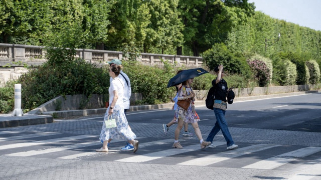 Des piétons traversent la rue en se protégeant du soleil avec un parapluie et un chapeau par une chaude après-midi, à Paris, le 13 juin 2025.
