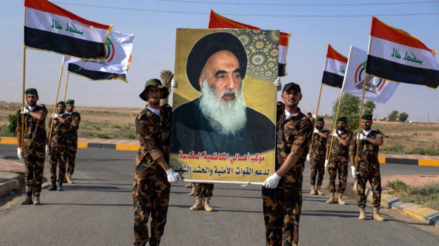 Des combattants des Hachd al-Chaabi, anciens paramilitaires intégrés aux forces irakiennes, portent des drapeaux nationaux et un portrait du Grand Ayatollah Ali al-Sistani, religieux chiite musulman de leur pays, alors qu'ils participent à un défilé marquant le 9e anniversaire de leur fondation, dans la région d'al-Hadar, dans le nord de l'Irak, le 22 juin 2023.