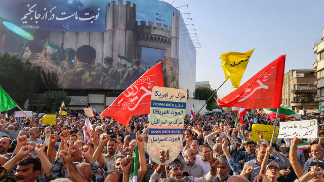 Des Iraniens brandissent des drapeaux et des pancartes lors d'un rassemblement de protestation contre l'attaque américaine contre l'Iran sur la place Enghelab à Téhéran, le 22 juin 2025. Le président iranien Masoud Pezeshkian a condamné les frappes américaines sur les sites nucléaires le 22 juin, déclarant dans sa première réponse que l'attaque révélait que Washington était "derrière" la campagne militaire d'Israël dans la République islamique.