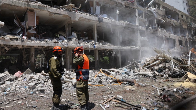 Les forces de sécurité israéliennes regardent une pelleteuse déblayer les décombres d'un bâtiment détruit sur le site d'une frappe iranienne qui a touché un quartier résidentiel dans la zone de Ramat Aviv à Tel Aviv, le 22 juin 2025.
