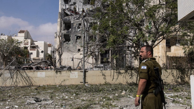 Un membre des forces de sécurité israéliennes monte la garde alors que des sauveteurs recherchent des victimes dans les décombres d'un bâtiment touché par un missile iranien à Beersheba, dans le sud d'Israël, le 24 juin 2025. Le président américain Donald Trump a annoncé un processus de cessez-le-feu progressif de 24 heures commençant vers 4 heures GMT le 24 juin, qu'Israël a déclaré avoir accepté. L'Iran n'a pas formellement accepté le cessez-le-feu.