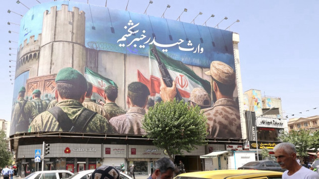 Des personnes passent devant une immense bannière sur la place Enghelab (Révolution), à Téhéran, le 24 juin 2025. Le 24 juin, les médias iraniens ont annoncé qu'une frappe israélienne dans le nord du pays avait tué neuf personnes, avant l'annonce par le président américain du début d'un cessez-le-feu entre Israël et l'Iran.