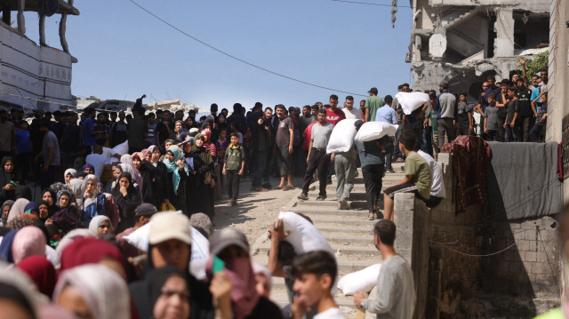 Des hommes palestiniens emportent des sacs de farine tandis que d'autres attendent devant un point de distribution mis en place par l'organisation indépendante Save Youth Future Society (SYFS), en coordination avec le Programme alimentaire mondial des Nations unies (PAM), dans la ville de Gaza, le 26 juin 2025.