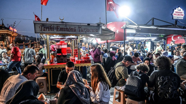 Un vendeur ambulant vend des cornichons et du jus de cornichon alors que des personnes mangent des cornichons dans le quartier d'Eminonu à Istanbul.