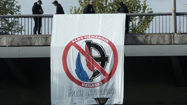 Un groupe de personnes installe une banderole représentant le signe du Front national (FN) (à gauche) et la croix celtique néo-nazie (à droite) avec un panneau d'interdiction indiquant « Sortez d'ici » alors qu'ils participent à une manifestation devant le lieu où la députée du parti d'extrême droite Front national (FN) Marion Maréchal Le Pen donne un meeting de campagne avant les élections présidentielles françaises à Bayonne, le 11 avril 2017.
