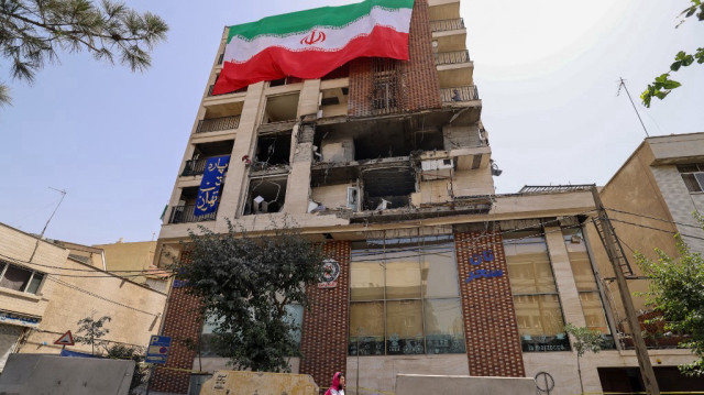 Une femme passe devant un immeuble résidentiel touché par une frappe israélienne et recouvert d'un grand drapeau iranien, à Téhéran, le 25 juin 2025.