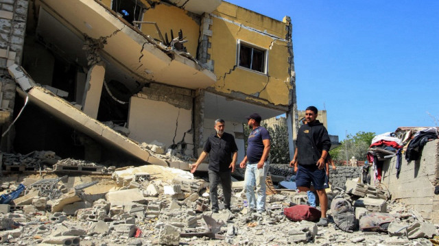 Des personnes inspectent les décombres devant un bâtiment gravement endommagé sur le site d'une frappe aérienne israélienne nocturne dans le village méridional libanais d'Aïn Qana, le 6 juin 2025. 