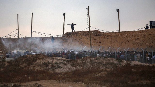Des membres d'une société de sécurité privée américaine, engagée par la Fondation humanitaire de Gaza (GHF), un groupe d'aide privé soutenu par les États-Unis avec lequel l'ONU refuse de travailler pour des raisons de neutralité, dirigent des Palestiniens déplacés qui se rassemblent pour recevoir des fournitures de secours dans un centre de distribution au centre de la bande de Gaza, le 8 juin 2025, alors que des bombes fumigènes sont tirées par les troupes israéliennes.