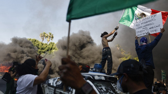 Un manifestant brandit un drapeau mexicain au-dessus d'une voiture Waymo en feu le 08 juin 2025 à Los Angeles, en Californie. Les tensions dans la ville restent vives après que l'administration Trump a fait appel à la Garde nationale contre la volonté des dirigeants de la ville, à la suite de deux jours d'affrontements avec la police lors d'une série de raids sur l'immigration.