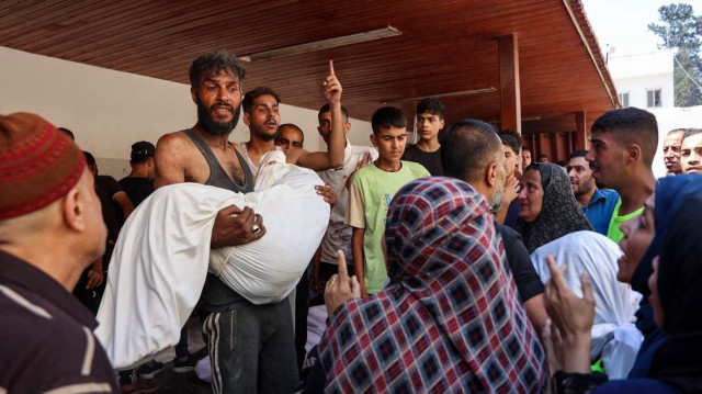 Un Palestinien porte le corps d'une personne tuée lors d'une frappe israélienne sur un entrepôt de distribution d'aide humanitaire dans le quartier de Sabra, dans la ville de Gaza, au centre de la bande de Gaza, dans l'enceinte de l'hôpital arabe Al-Ahli, également connu sous le nom d'hôpital baptiste, le 30 juin 2025.
