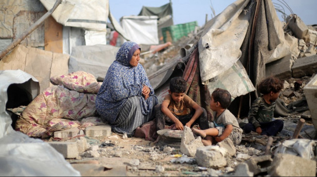 Une femme palestinienne et des enfants sont assis au milieu des décombres après une frappe israélienne dans le camp de réfugiés de Bureij, dans le centre de la bande de Gaza, le 10 juillet 2025.