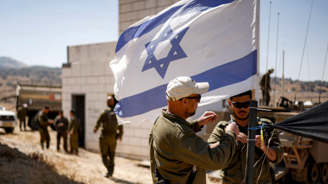 Des soldats de l'armée israélienne ajoutent des attaches au mât d'un drapeau israélien flottant dans une zone spéciale pour les exercices, lors d'un exercice militaire sur le plateau du Golan annexé par Israël, le 8 juillet 2025.