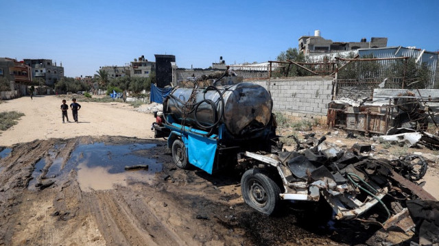 Des garçons se tiennent près d'une citerne d'eau mobile détruite par un bombardement israélien dans le camp de réfugiés palestiniens de Nuseirat, dans le centre de la bande de Gaza, le 14 juillet 2025.