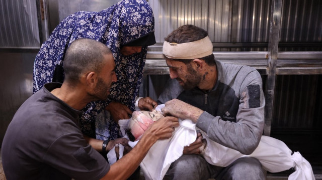 Les Palestiniens pleurent le corps enveloppé d'un enfant, tué lors des frappes israéliennes de la nuit, dans la morgue de l'hôpital Al-Shifa dans la ville de Gaza, le 15 juillet 2025.