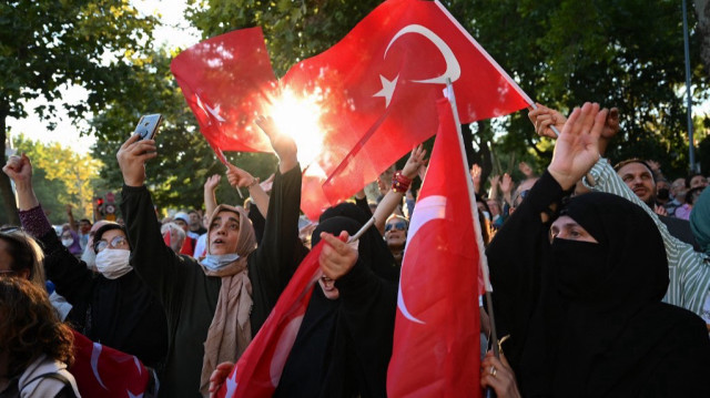 Des partisans applaudissent et agitent des drapeaux nationaux turcs pendant le discours du président turc lors d'un rassemblement dans le quartier de Fatih à Istanbul, le 15 juillet 2022, lors de la Journée de la démocratie et de l'unité nationale de la Turquie commémorant le coup d'État manqué de 2016.