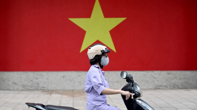 Une femme circulant à moto devant un mur peint du drapeau national vietnamien à Hanoï.