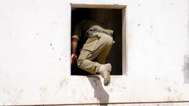 Un soldat de l'armée israélienne entre par l'ouverture d'une fenêtre dans un bâtiment dans une zone spéciale pour les exercices pendant un exercice militaire dans les hauteurs du Golan annexées par Israël, le 8 juillet 2025.