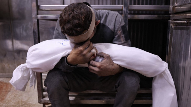 Un Palestinien pleure en tenant le corps enveloppé d'un enfant, tué lors des frappes israéliennes de la nuit, dans la morgue de l'hôpital Al-Shifa de la ville de Gaza, le 15 juillet 2025.