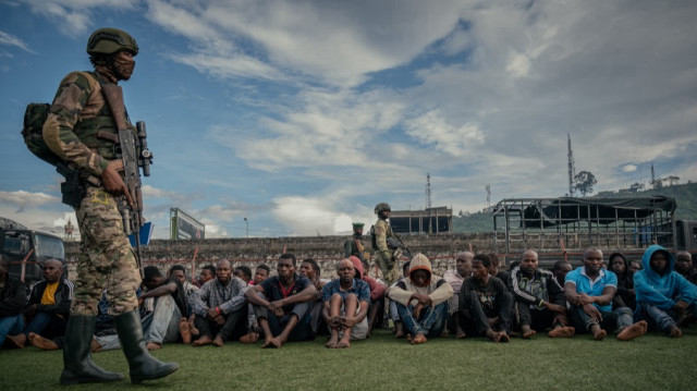 Un soldat du M23 surveille un groupe d'une centaine de combattants des Forces démocratiques pour la libération du Rwanda (FDLR), de Wazalendo et des Forces armées de la République démocratique du Congo (FARDC) au Stade de l'Unité, lors de leur présentation par le colonel Willy Ngoma à Goma, le 10 mai 2025.