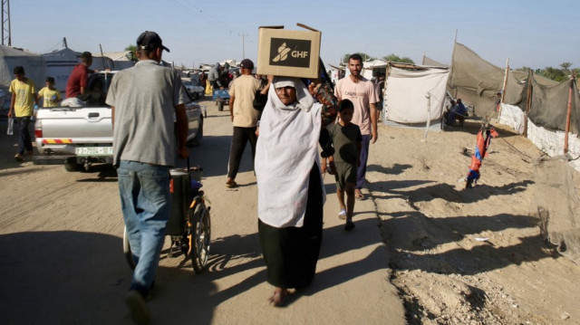 Une Palestinienne porte un sac d'aide humanitaire sur la tête alors qu'elle se rend dans le quartier de Mawasi à Rafah, le 24 juillet 2025, après avoir reçu de l'aide humanitaire dans un centre de distribution situé dans le sud de la bande de Gaza.
