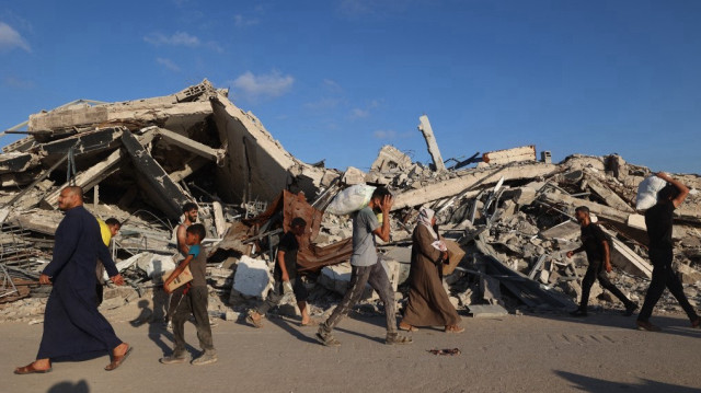 Des personnes, certaines portant des colis d'aide, marchent sur la route de Salah al-Din près du camp de réfugiés de Nusseirat dans le centre de la bande de Gaza, utilisée par les Palestiniens à la recherche de nourriture pour atteindre un point de distribution d'aide mis en place par la Fondation humanitaire de Gaza (GHF), le 25 juin 2025.