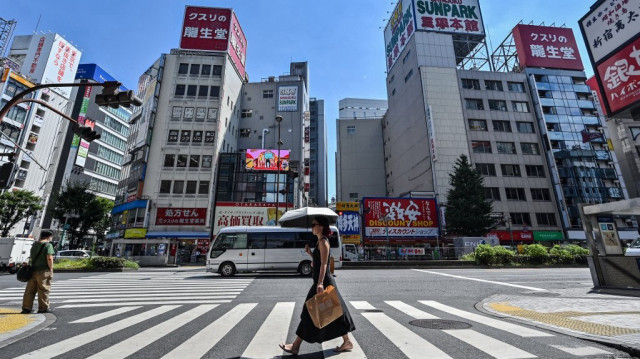 Une femme porte un parapluie pour se protéger du soleil tandis que des piétons traversent une rue dans le quartier des divertissements de Kabukicho, à Shinjuku, dans le centre de Tokyo, le 29 juillet 2025.